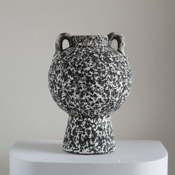 Speckled black and white ceramic vase on a plain background